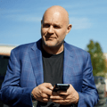 Saul Zenkevicius, commercial real estate investor, in a blue plaid blazer holding a phone outdoors