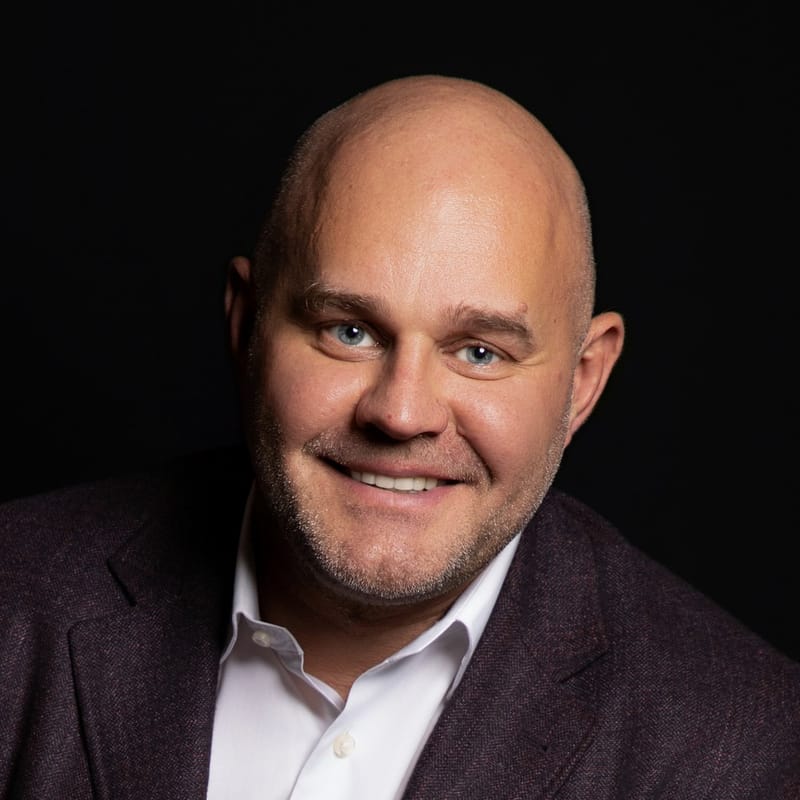 Saul Zenkevicius smiling in a dark tweed blazer